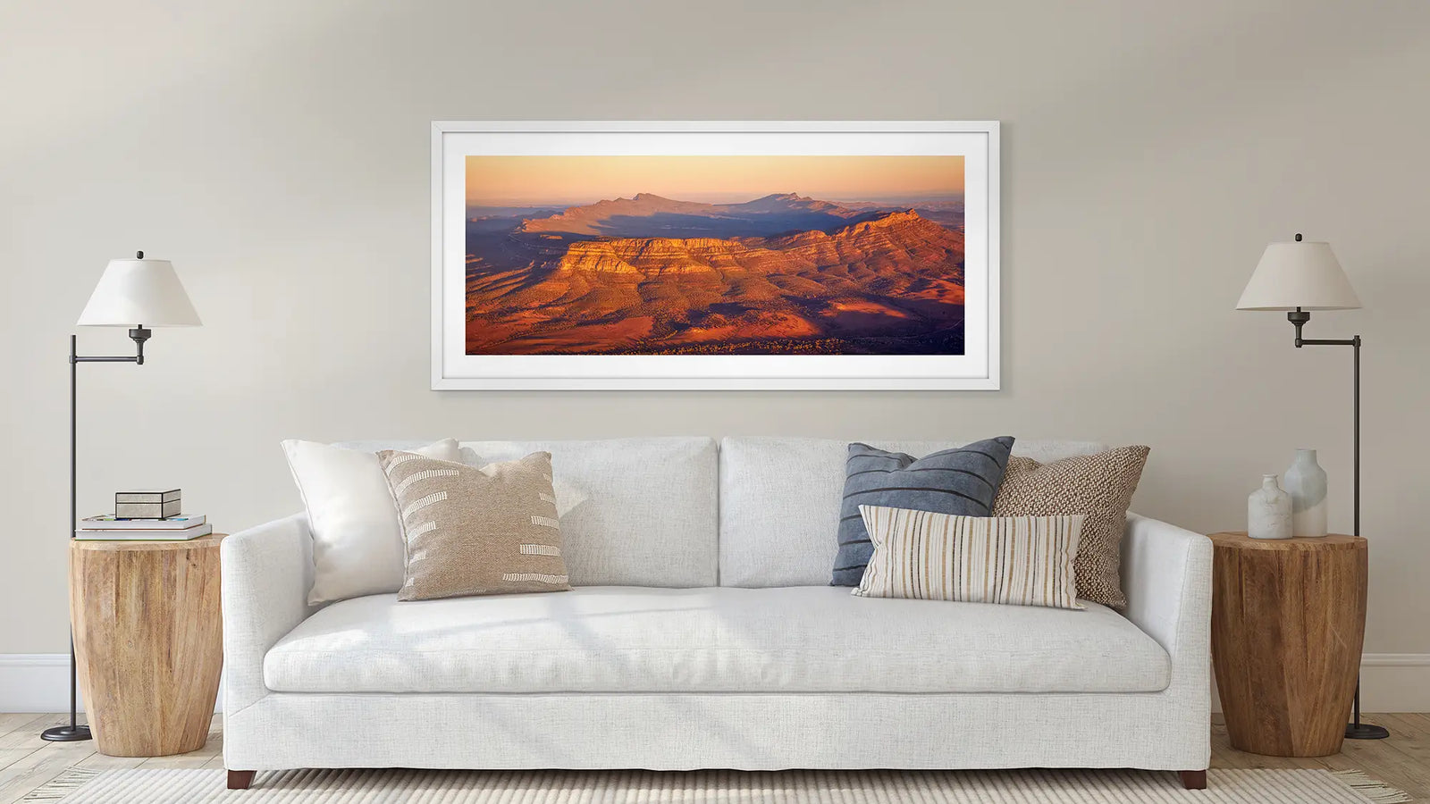 Framed landscape print with brown colour on a wall above a white sofa with decorative pillows.