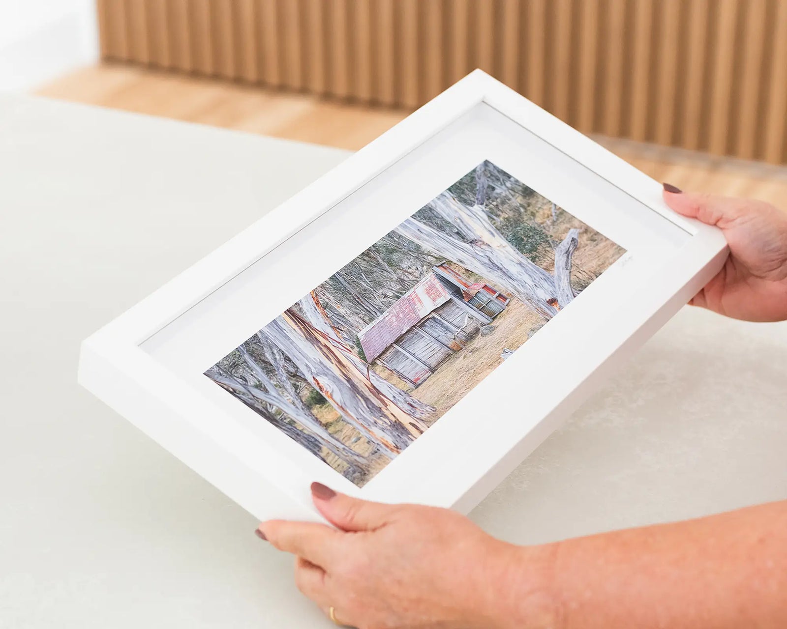 Framed photograph of Cascade Hut surrounded by gum trees on a plain background.