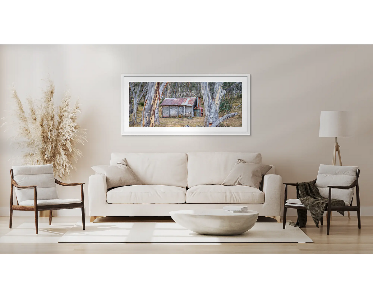 Abode Among the Gum Trees. Wall art print with white frame of Cascade Hut, Kosciuszko National Park, hung above a couch.