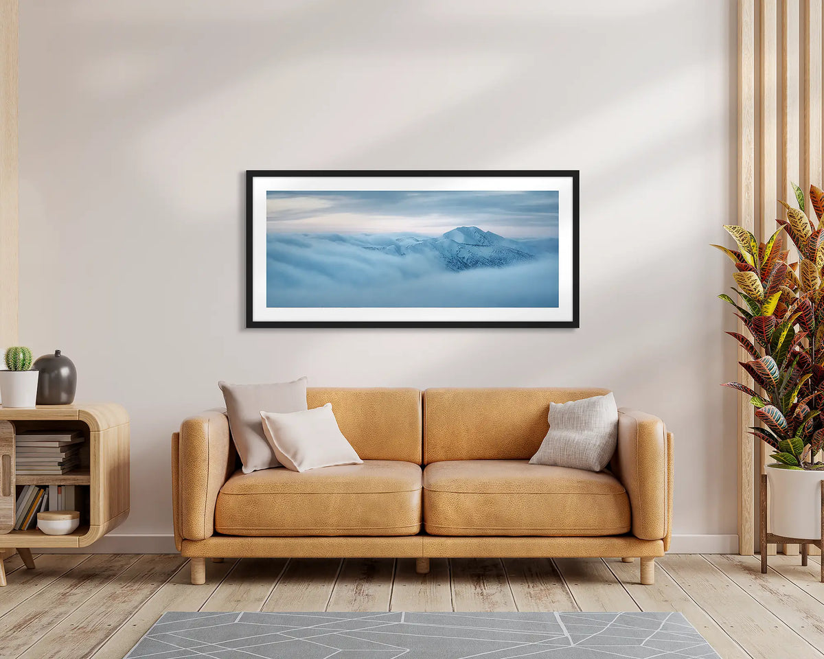Above It All. Wall art print of Mount Feathertop surrounded by clouds, with a black frame, hung above a leather couch. 