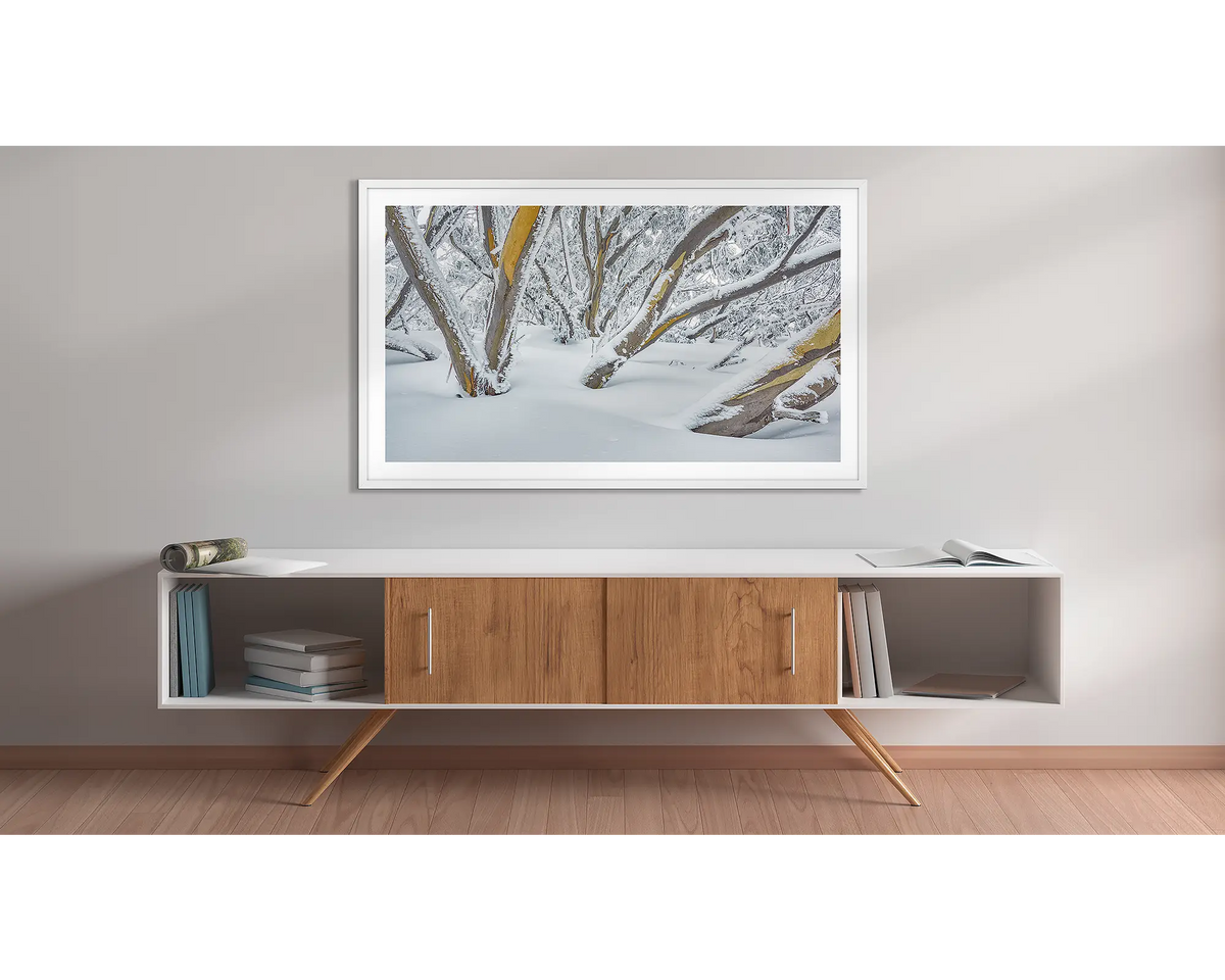 After the Storm. Wall art print of snow gums on Mount Hotham, covered in snow, framed with a white frame, and hung above a side table. 