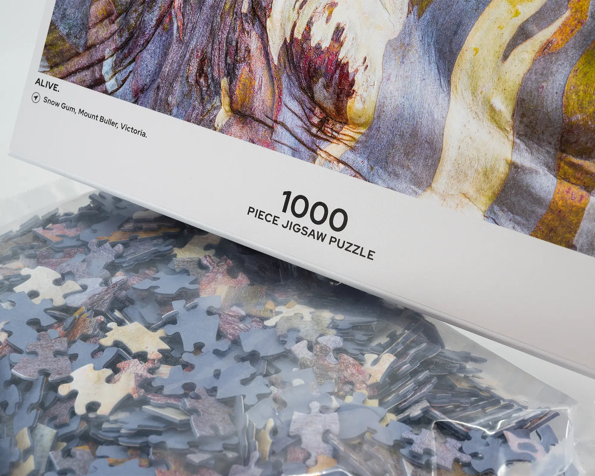 Alive. 1000 piece abstract jigsaw puzzle of colourful snow gum bark patterns, showing puzzle pieces.