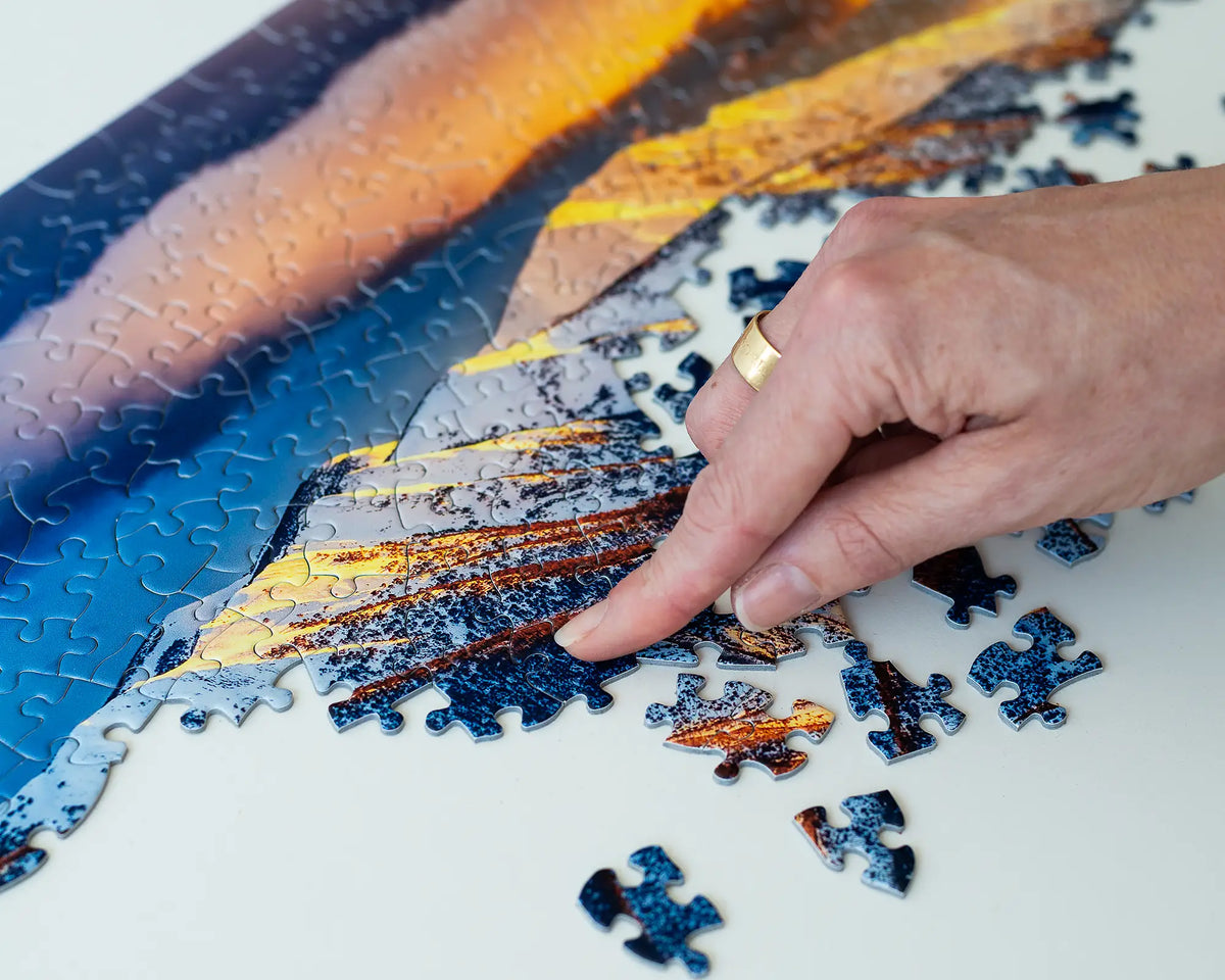 Alpine Magic 1000 piece jigsaw puzzle being made with female hand placing jigsaw piece on Mount Feathertop section.