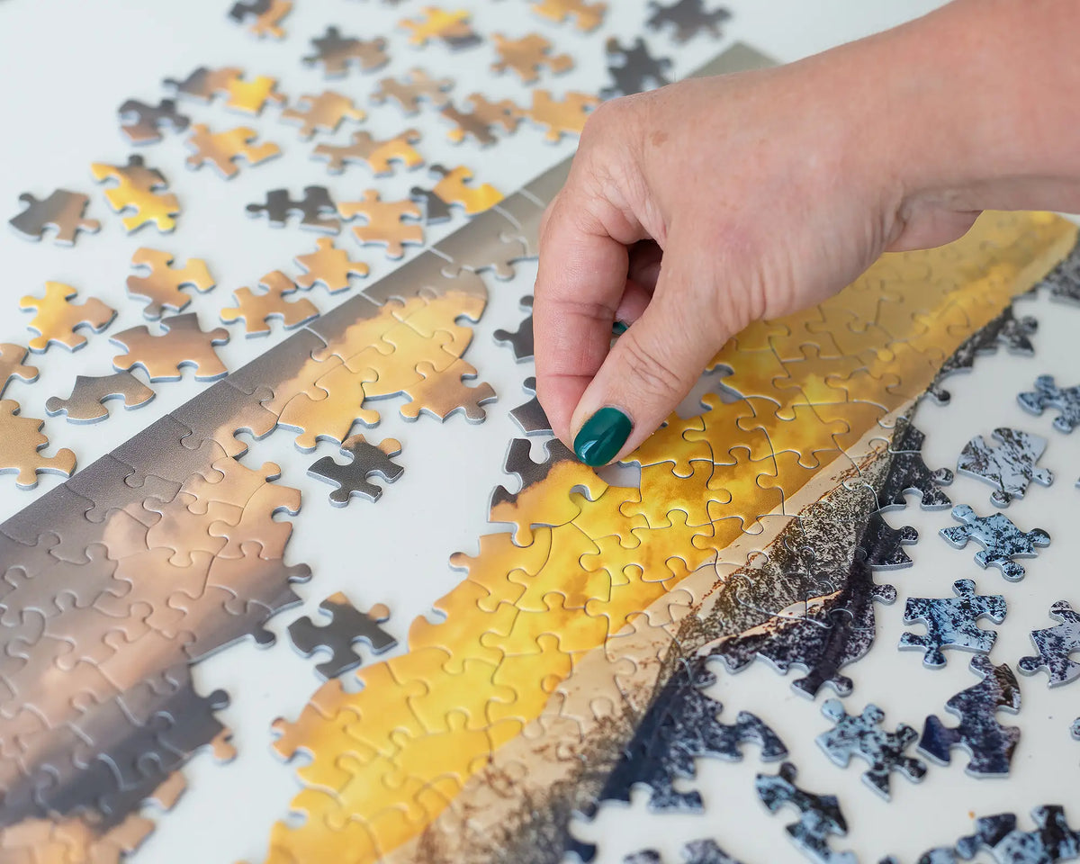 Alpine Magic 1000 piece jigsaw puzzle being made, with female hand placing jigsaw piece.