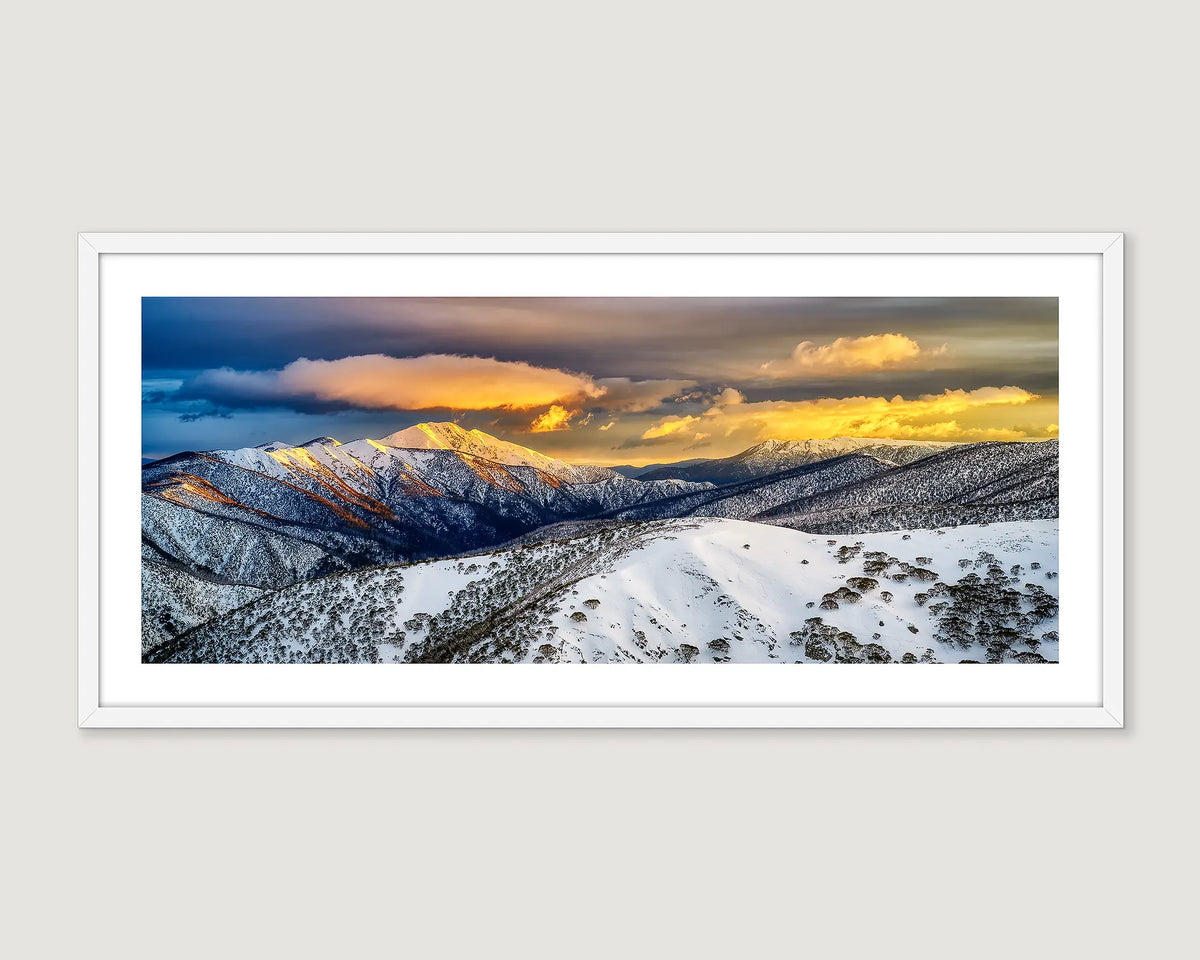 Framed photographic print of rising sun casting gold over the snowy peaks of Mount Feathertop. 