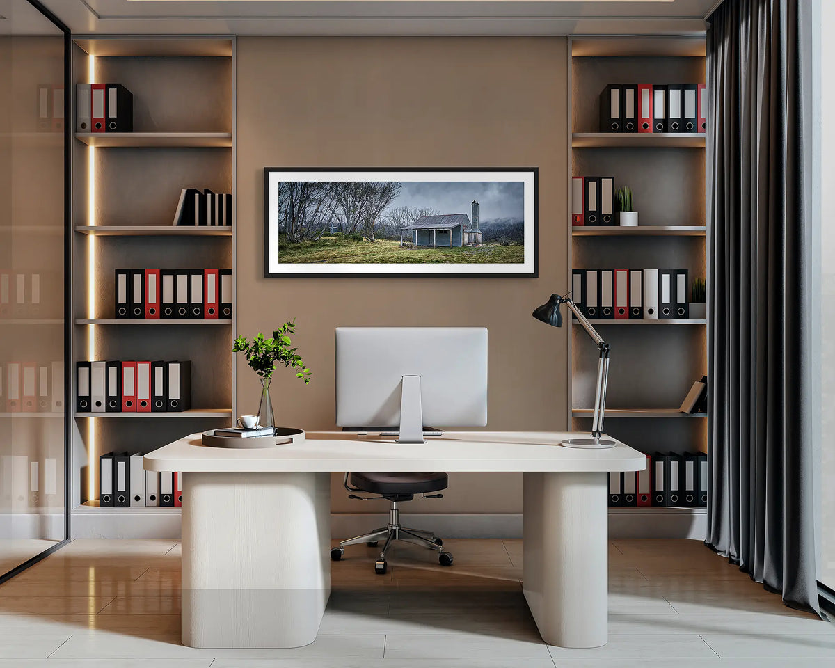 Alpine Retreat. Bradley and O&#39;Briens hut wall art print, with a black frame, hung behind an office desk. 