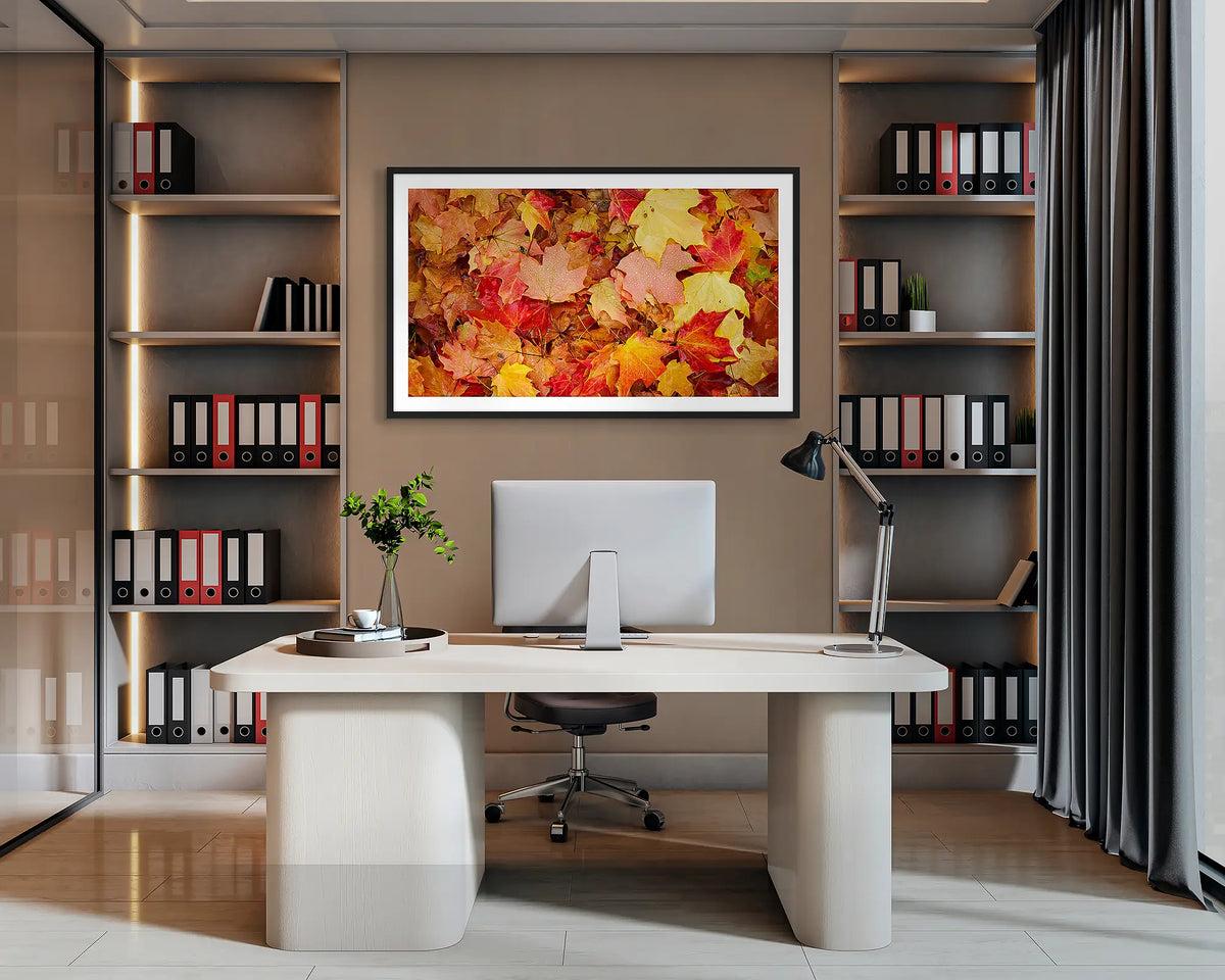 Autumn Layers. Wall art print of autumn leaves in Bright, Victoria, with a black frame, hanging behind a desk in a corporate office. 