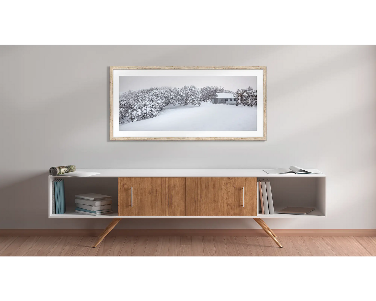 Awaken. Federation Hut with fresh snow wall art print with a timber frame hung above a side table. 