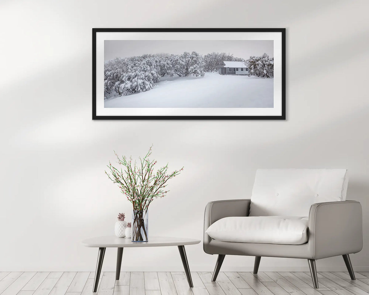 Awaken. Wall art print of a federation hut with fresh snow framed in  black frame and hung in a waiting area. 