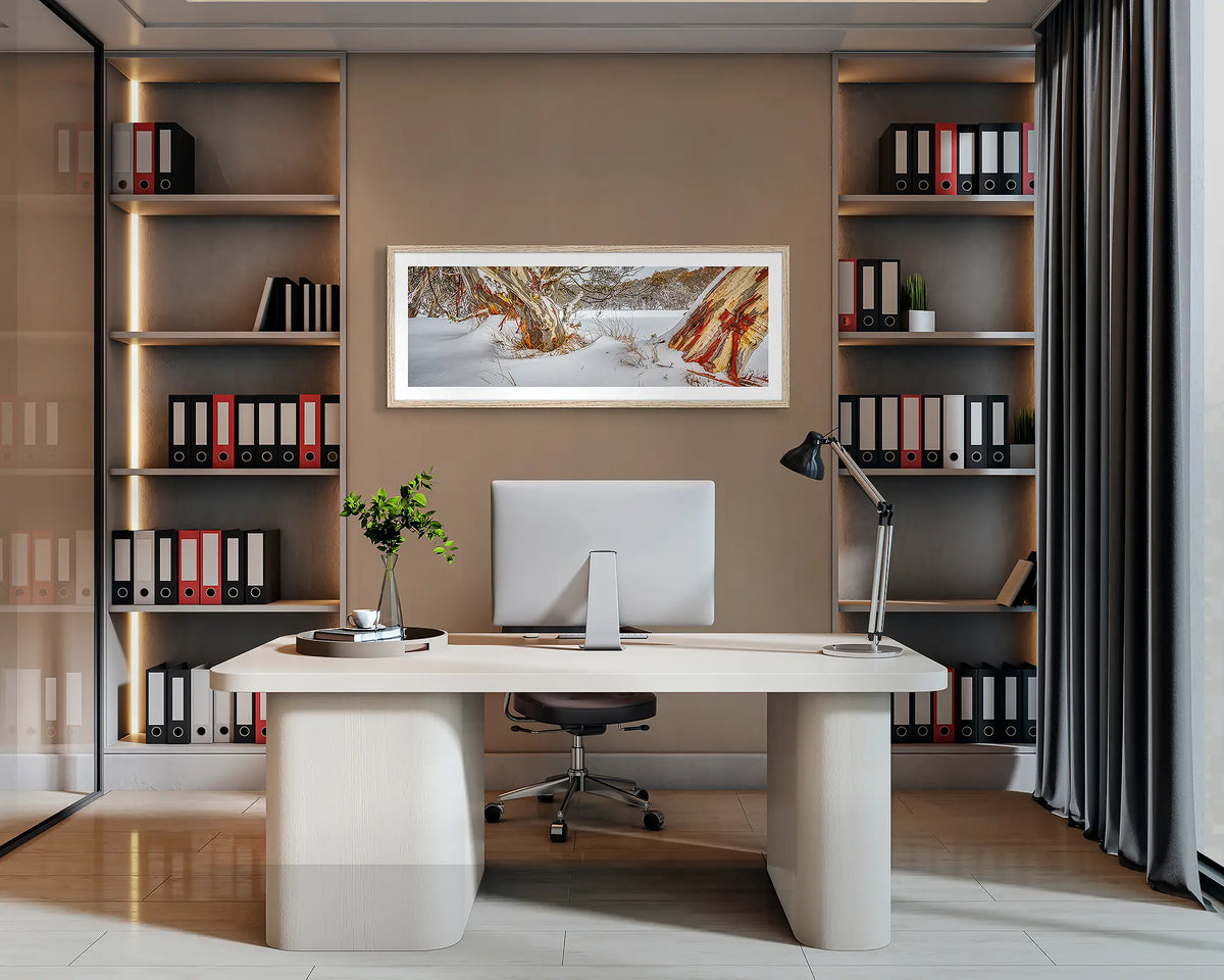 Back Country. Snow gum in a snow, panoramic wall art print, with a Tasmanian Oak frame, hung behind an office desk. 