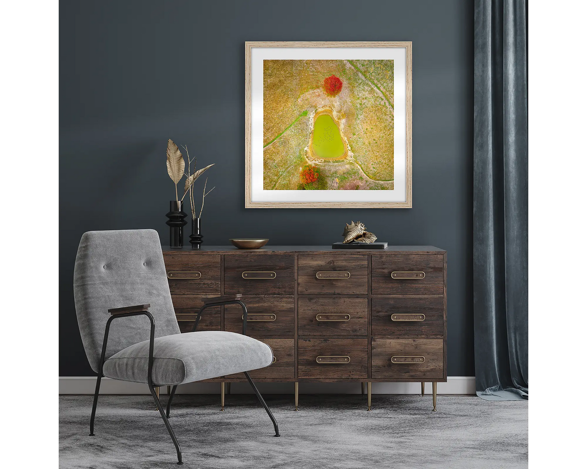 Ball Game. Wall art print with a timber frame, of an aerial view of a farm dam, hung in a room with dark walls. 