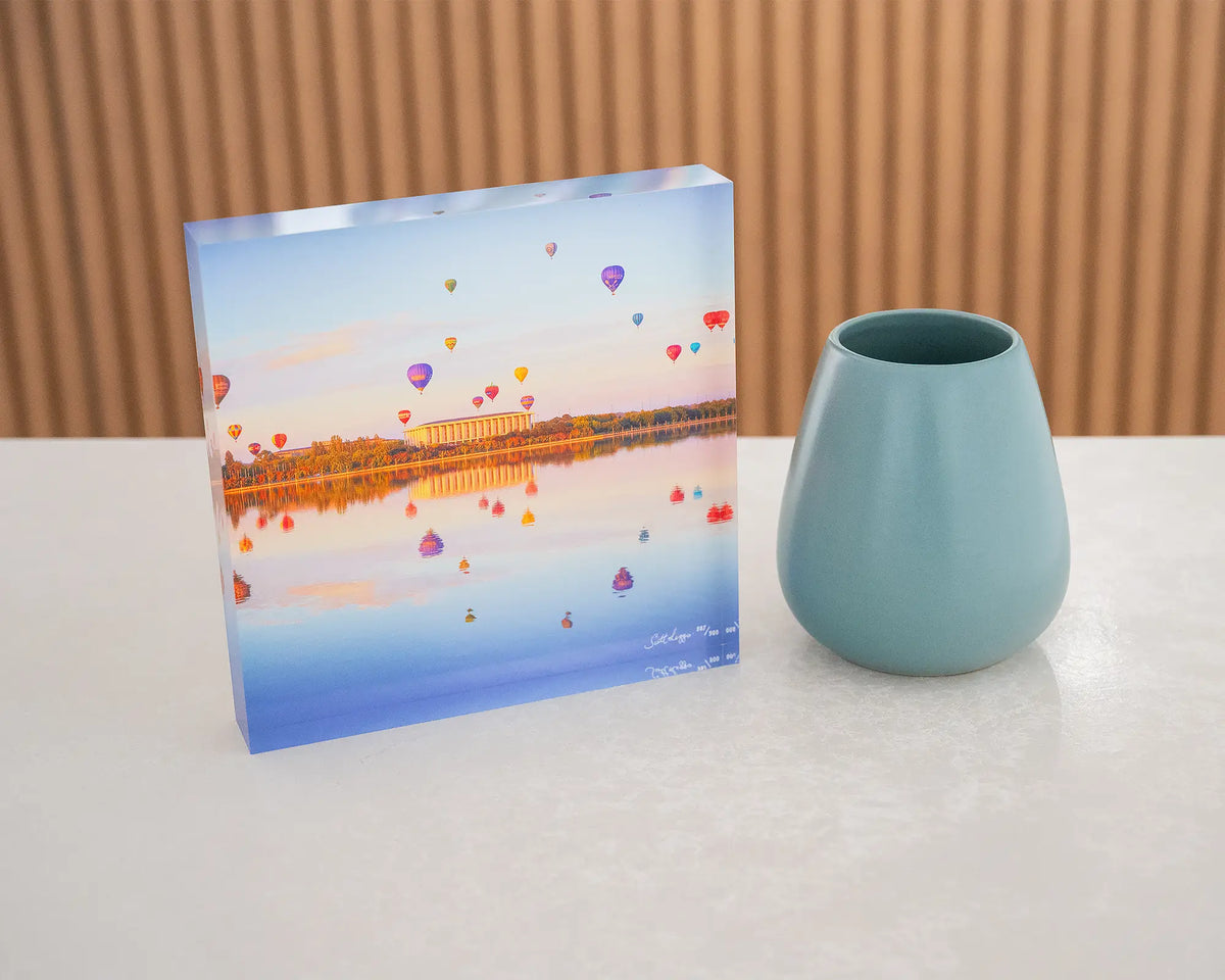 Balloon Spectacular. Acrylic block of hot air balloons over Lake Burley Griffin, styled on a desk with a small vase.