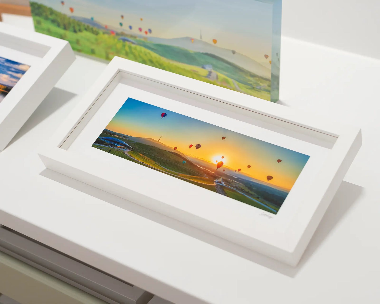 Framed photograph of a panoramic scene of hot air balloons over the arboretum at sunrise. 
