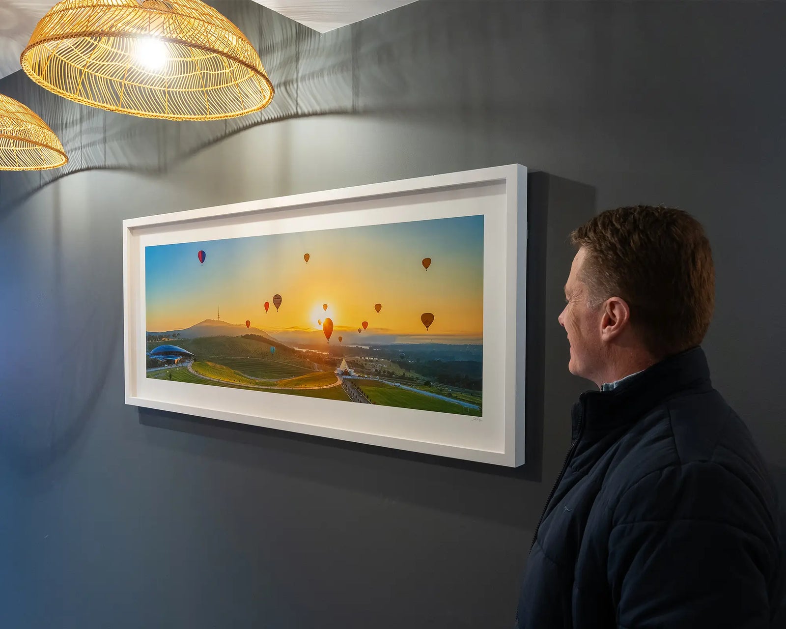 Framed photograph of a panoramic scene of hot air balloons over the arboretum at sunrise. 