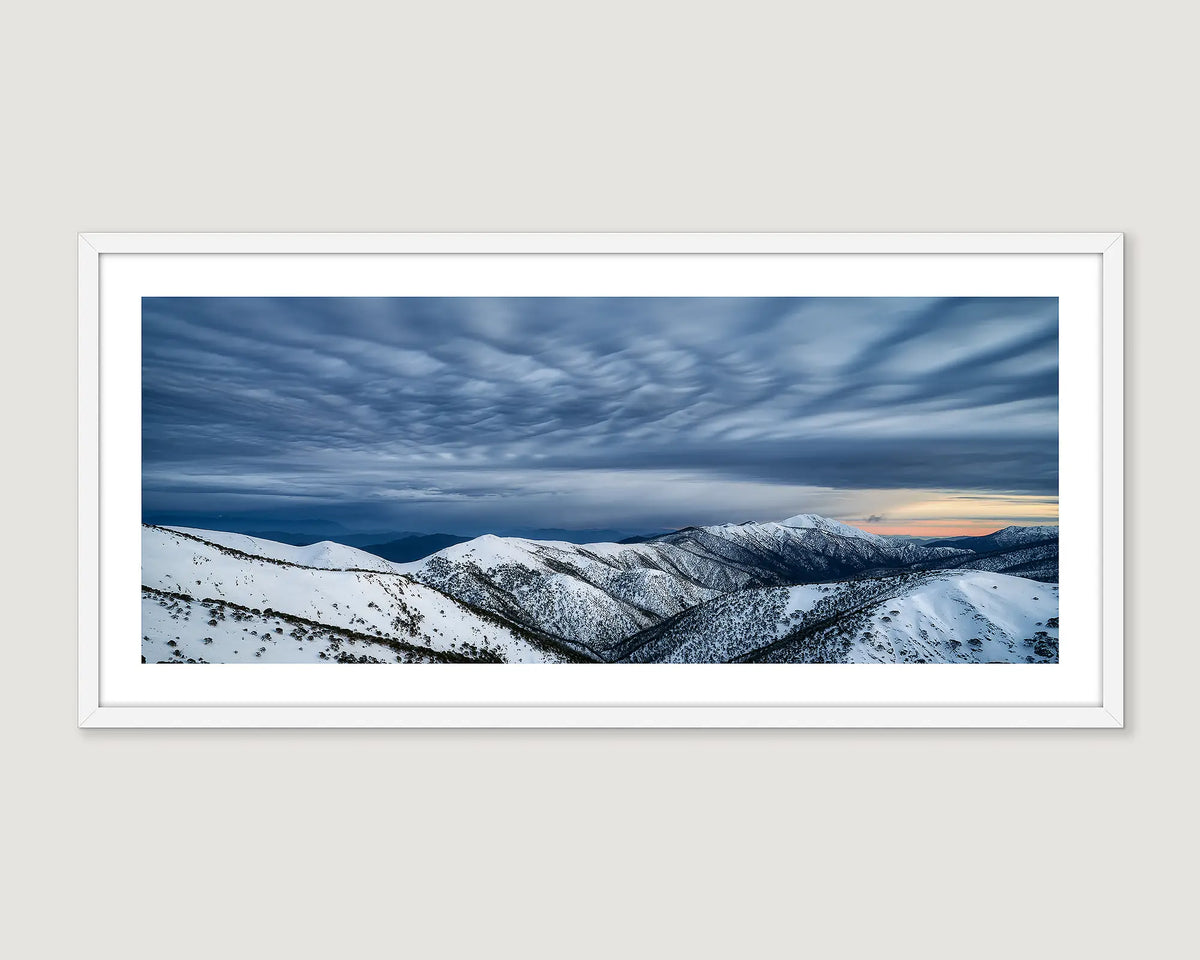Framed photograph of a sunrise behind storm clouds forming over Mount Feathertop, covered in snow. 