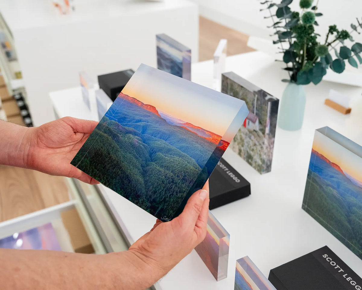 Breaking Dawn. Acrylic block of sun rising over Blue Mountains National Park, hand held in gallery with more acrylic blocks in background.