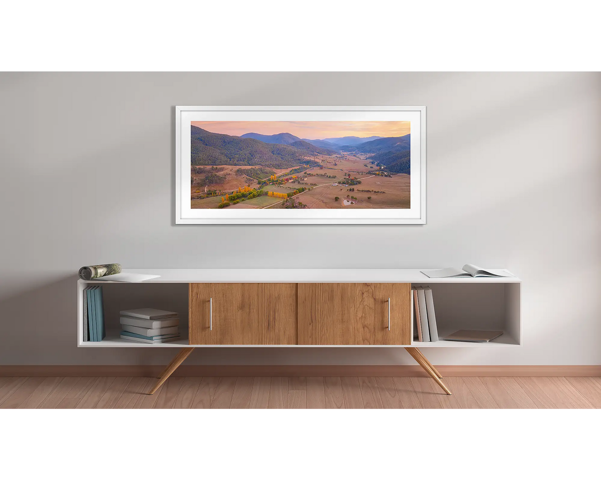 Brindabella Rise. Wall art print with a white frame, of a sunrise over the Brindabella valley, hung above a side table. 