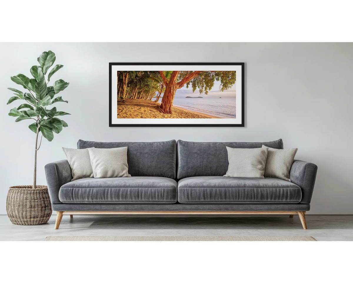 Cairns Escape. Framed wall art print of a sunrise on a tropical beach, with a black frame, hung above a couch.