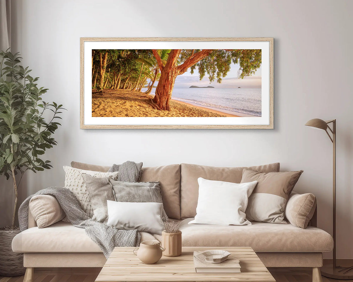 Cairns Escape. Wall art print of a sunrise on a tropical beach, framed with a Tasmanian Oak frame, hung above a couch.