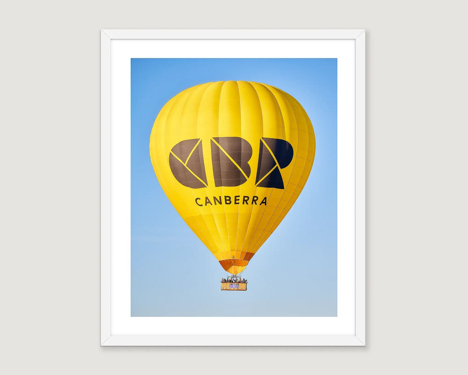 Framed wall art print of people in the yellow, CBR hot air ballon against a blue sky. 