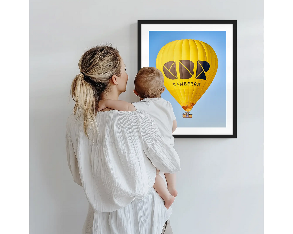 Canberra Bubble. Hot air balloon artwork with a black frame, being admired by a mother and baby. 