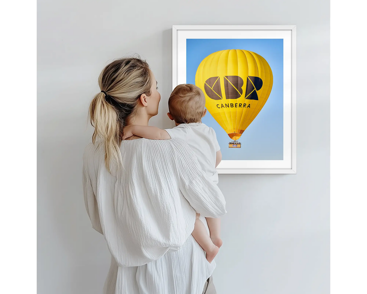 Canberra Bubble. Hot air balloon artwork with a white frame, being admired by a mother and baby. 