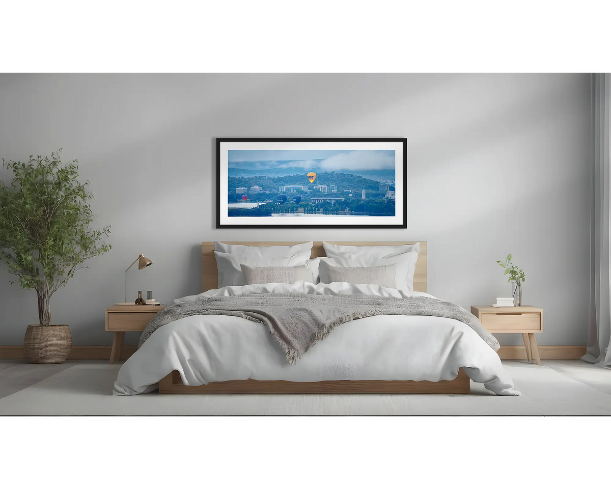 Canberra Rising. Wall art print of hot air balloons over Canberra, with a black frame, above a bed. 