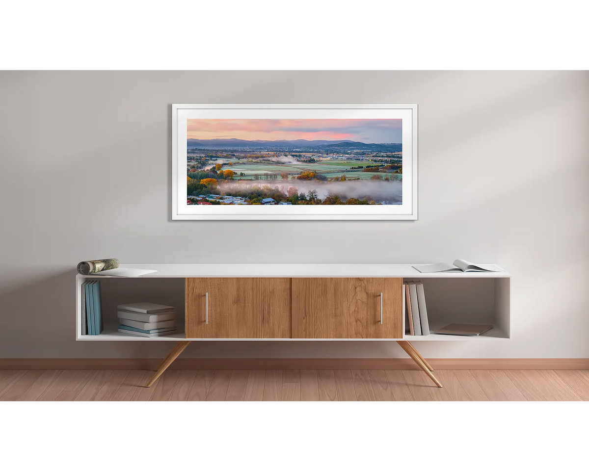 Canturf. Wall art print with a white frame, of a sunrise over Canturf, Fyshwick, Canberra, hung above a side table. 