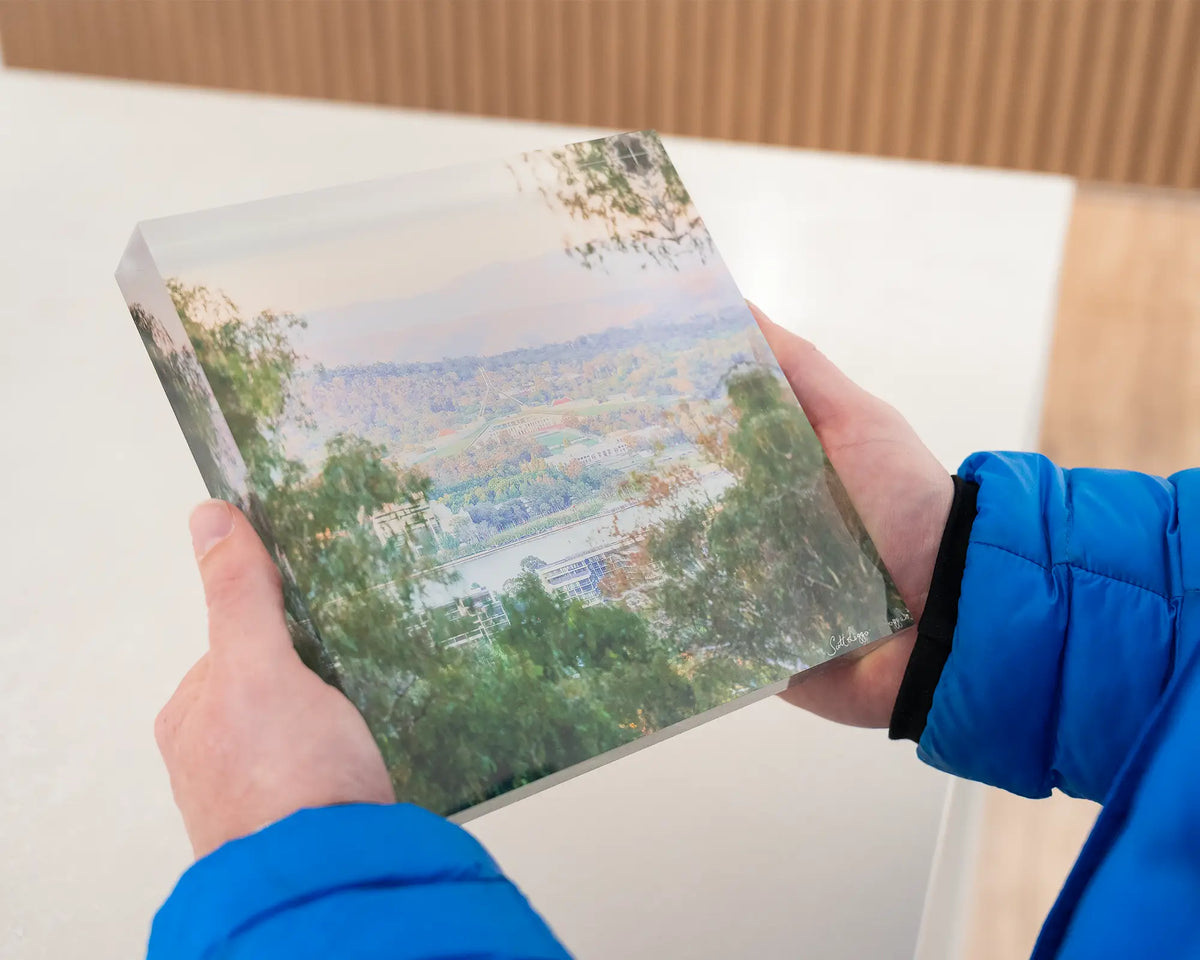 Capital View. Acrylic block views of Parliament House through gum trees, being held in hands.