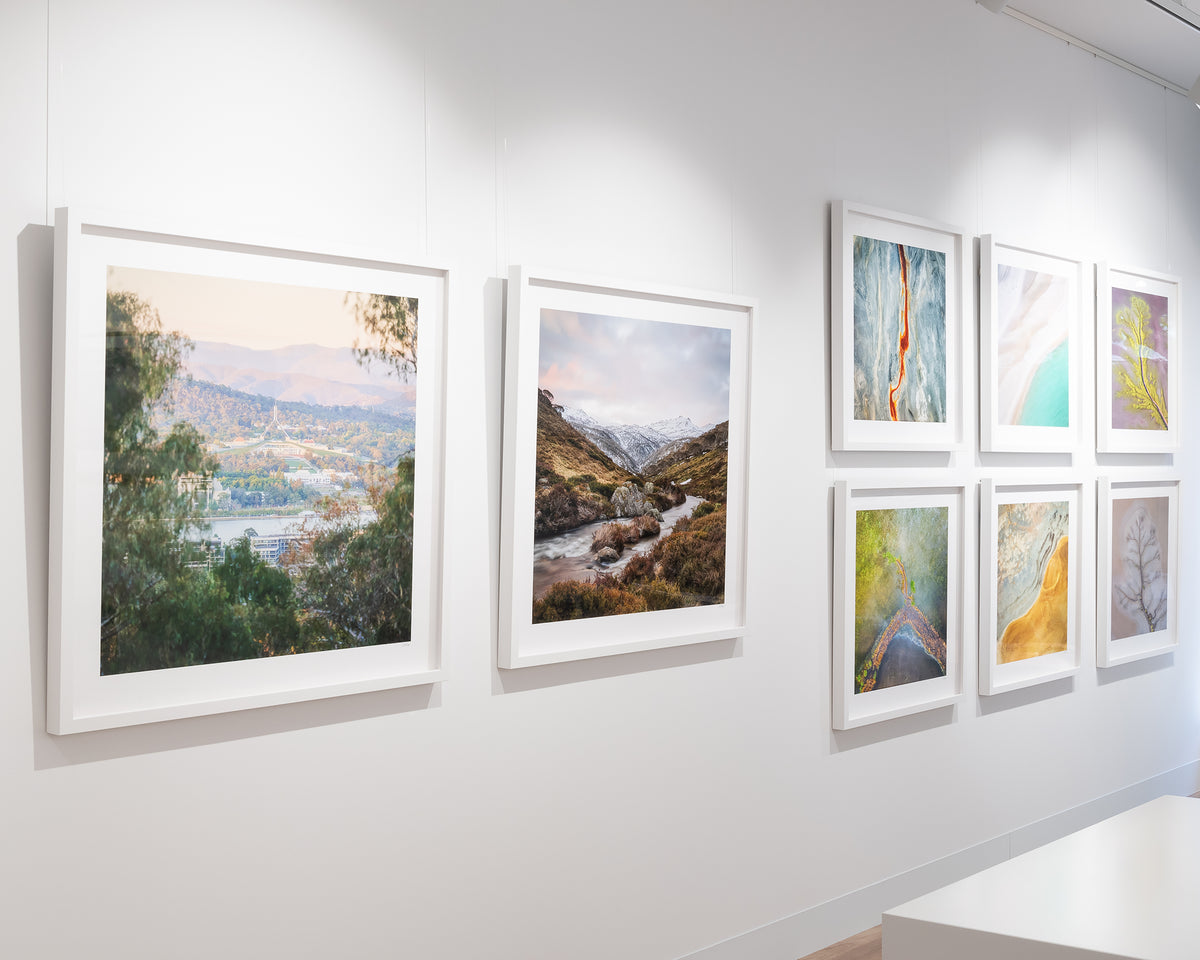 Capital View. Sunrise at Parliament House Canberra through bushland, with white frame, on display in gallery.