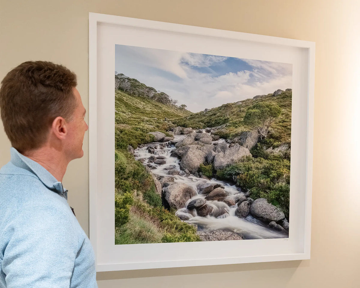 Cascade. Thredbo River, Pilot Wilderness area, Kosciuszko National Park, with white frame, on cream wall, and person admiring.