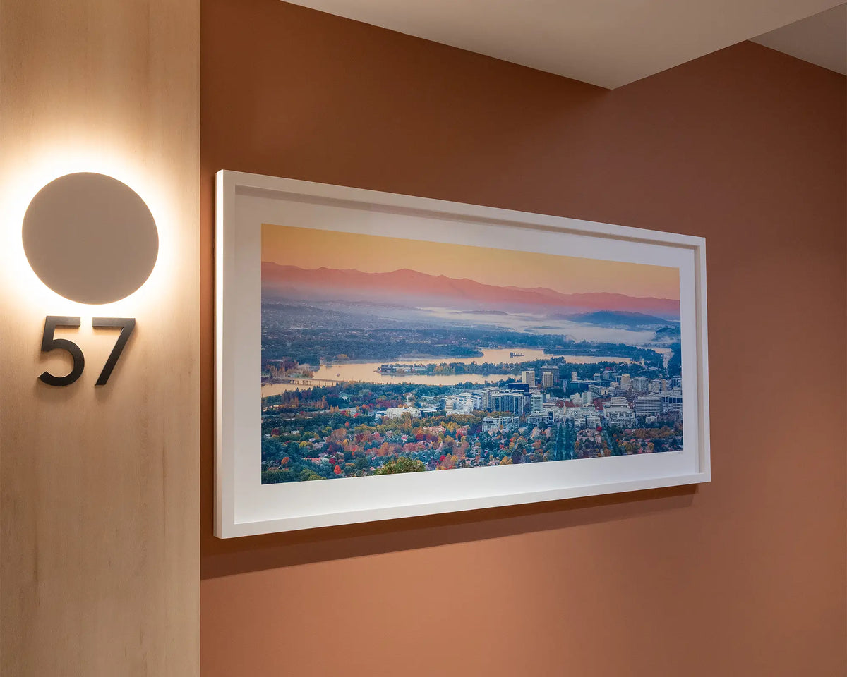 Civic Autumn. Sunrise over Canberra, with white frame, hung on terracotta coloured wall in apartment building.