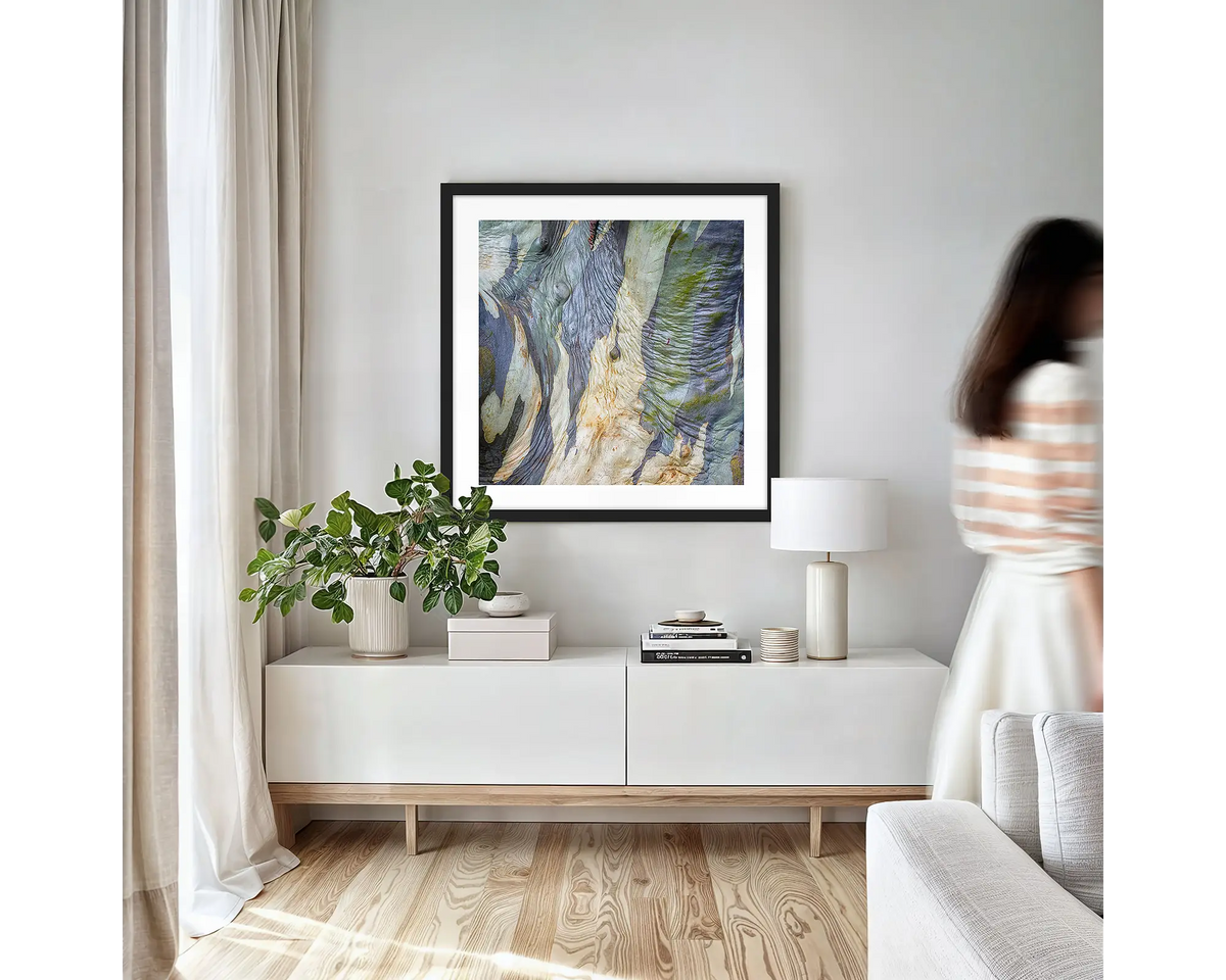 Continuity. Abstract wall art print of wrinkles in snow gum bark, with a black frame, hung on an apartment wall above a side table. 