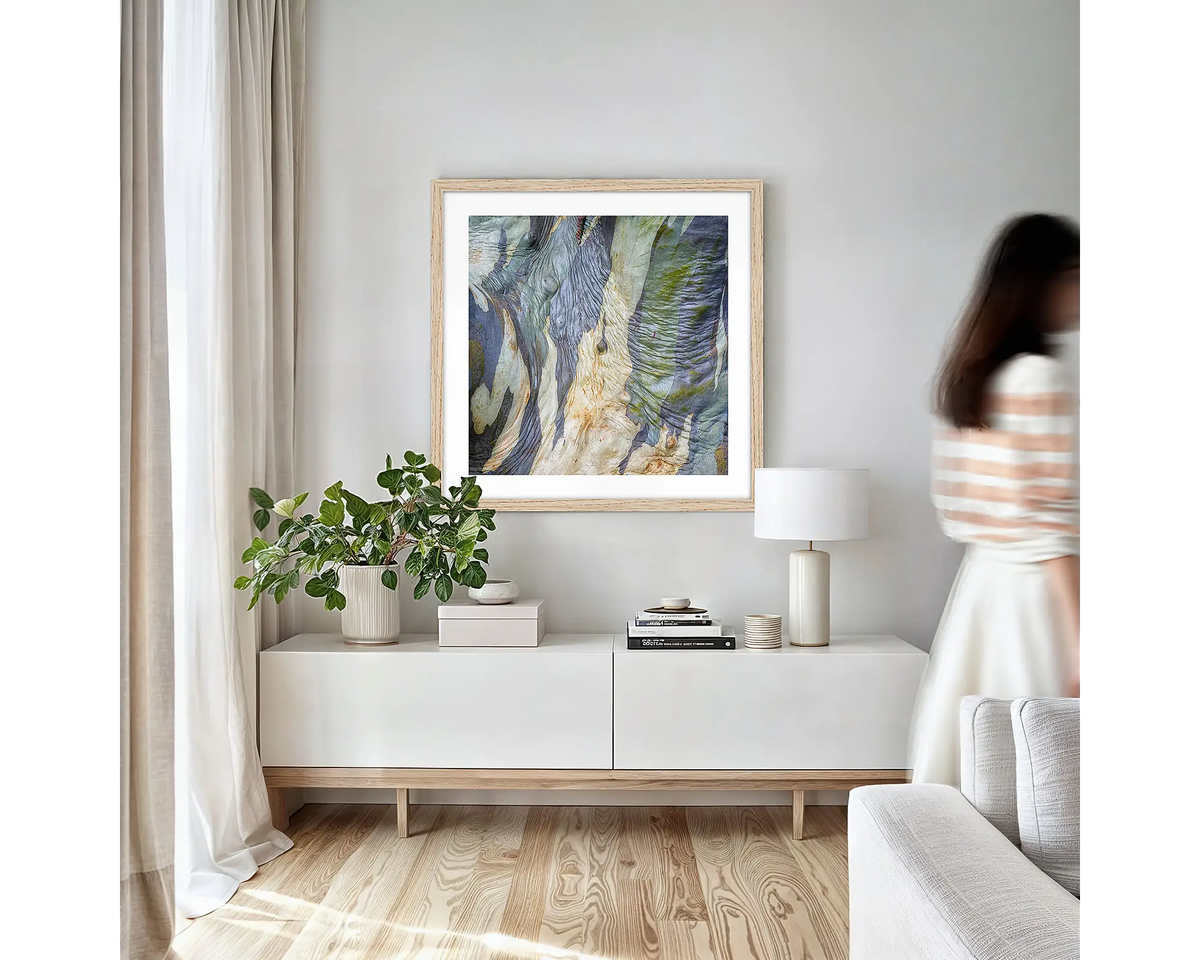 Continuity. Abstract wall art print of wrinkles in snow gum bark, with a timber frame, hung on an apartment wall above a side table. 