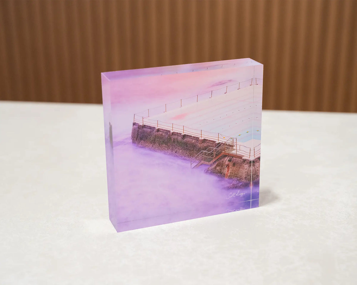 Corner. Acrylic block of sunrise at Bondi Icebergs, sitting on a desk.