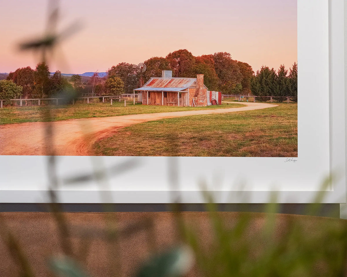 Country Charm. Rural farm wall art with white frame, close-up corner with greenery in foreground.