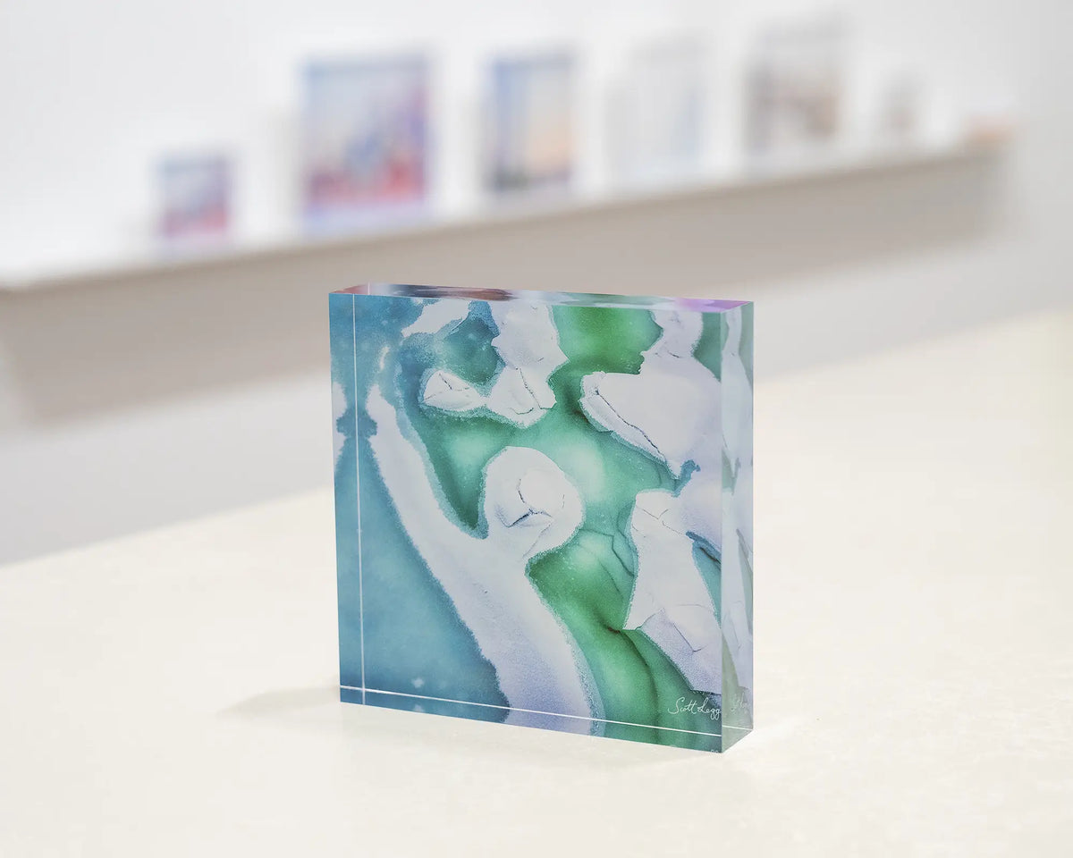 Cracked. Abstract acrylic block frozen Snowy River, Kosciuszko National Park, on gallery desk with display shelf behind.