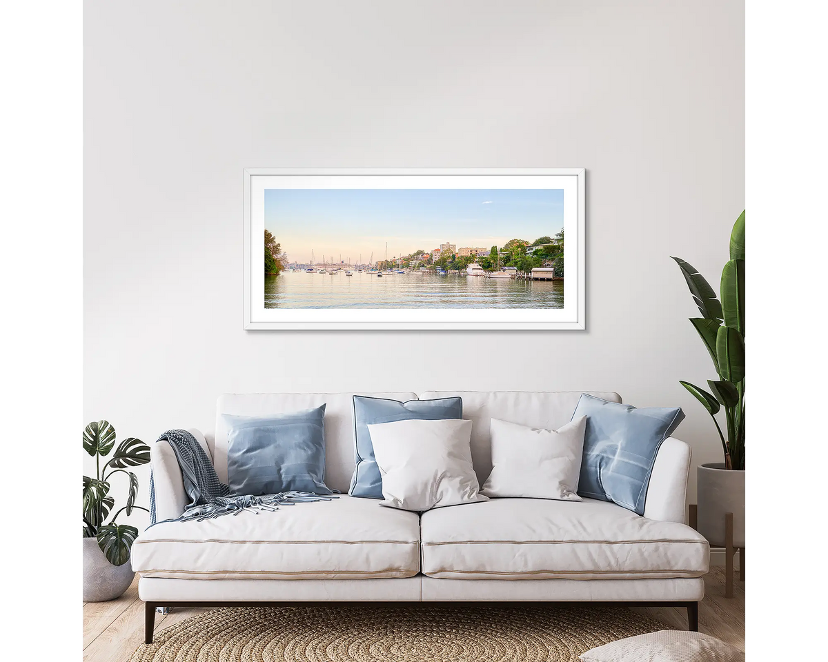 Cremorne Calm. Framed wall art print of Shell Cove, Sydney, with a white frame, hung above a couch. 