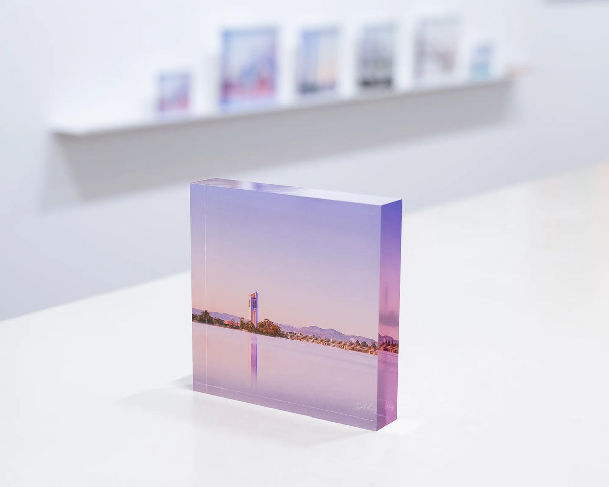 Crisp. Acrylic block of sunrise at the National Carillon, Canberra, on gallery desk with acrylic blocks on shelf behind.