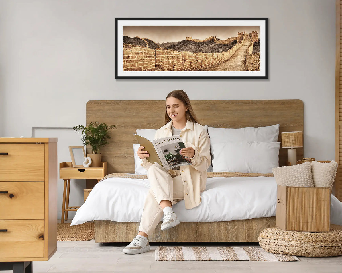Crumbling Wall. Great Wall of China wall art print, with a black frame hung above a bed, with a woman reading a magazine. 