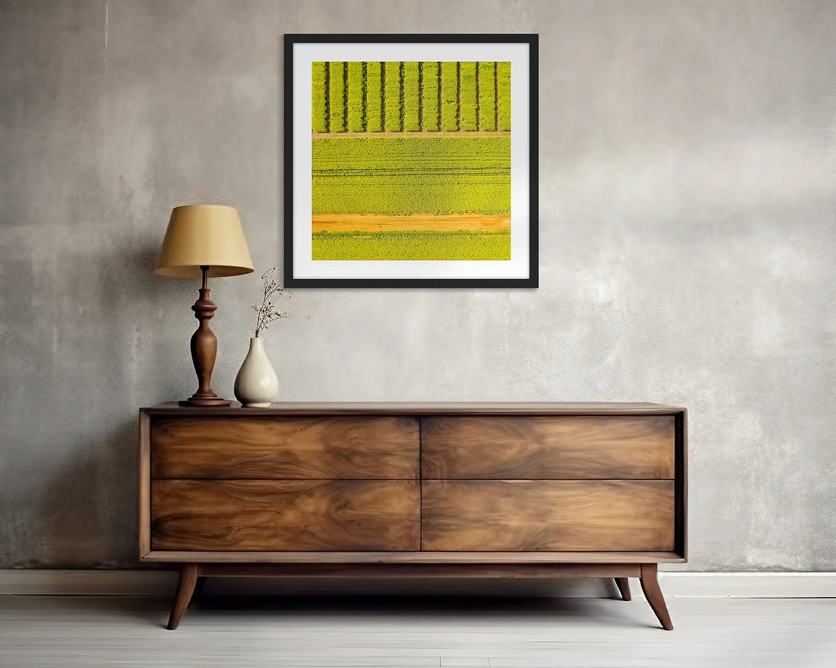 Cultivate. Square, canola wall art print, with a black frame, above a side table. 