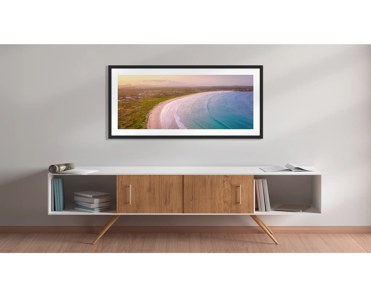 Curvature. Wall art print with a black frame, of a sunset over Broulee beach, New South Wales south coast, hung above a side table. 