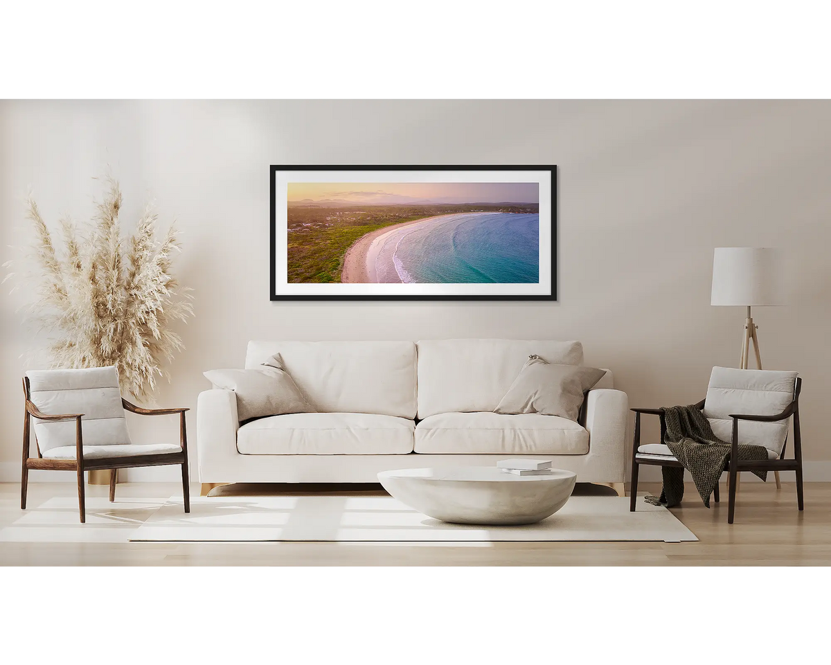 Curvature. Wall art print with a black frame, of a sunset over Broulee Beach, south coast, hung above a couch.