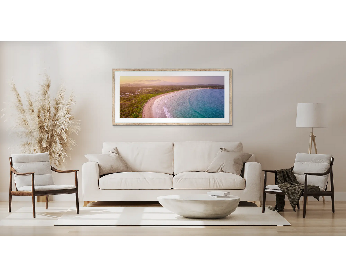 Curvature. Wall art print with timber frame of sunset over Broulee Beach, South Coast,  hung above a couch.