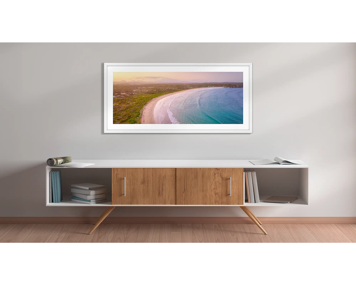 Curvature. Wall art print with a white frame, of a sunset over Broulee beach, New South Wales, south coast, hung above a side table. 