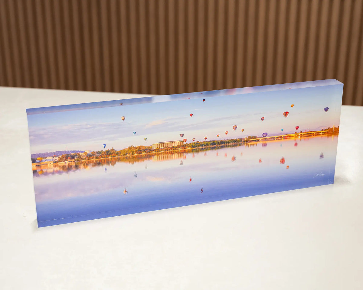Dawn Drifters. Acrylic block of the Balloon Spectacular over Lake Burley Griffin Canberra, placed on a desk.