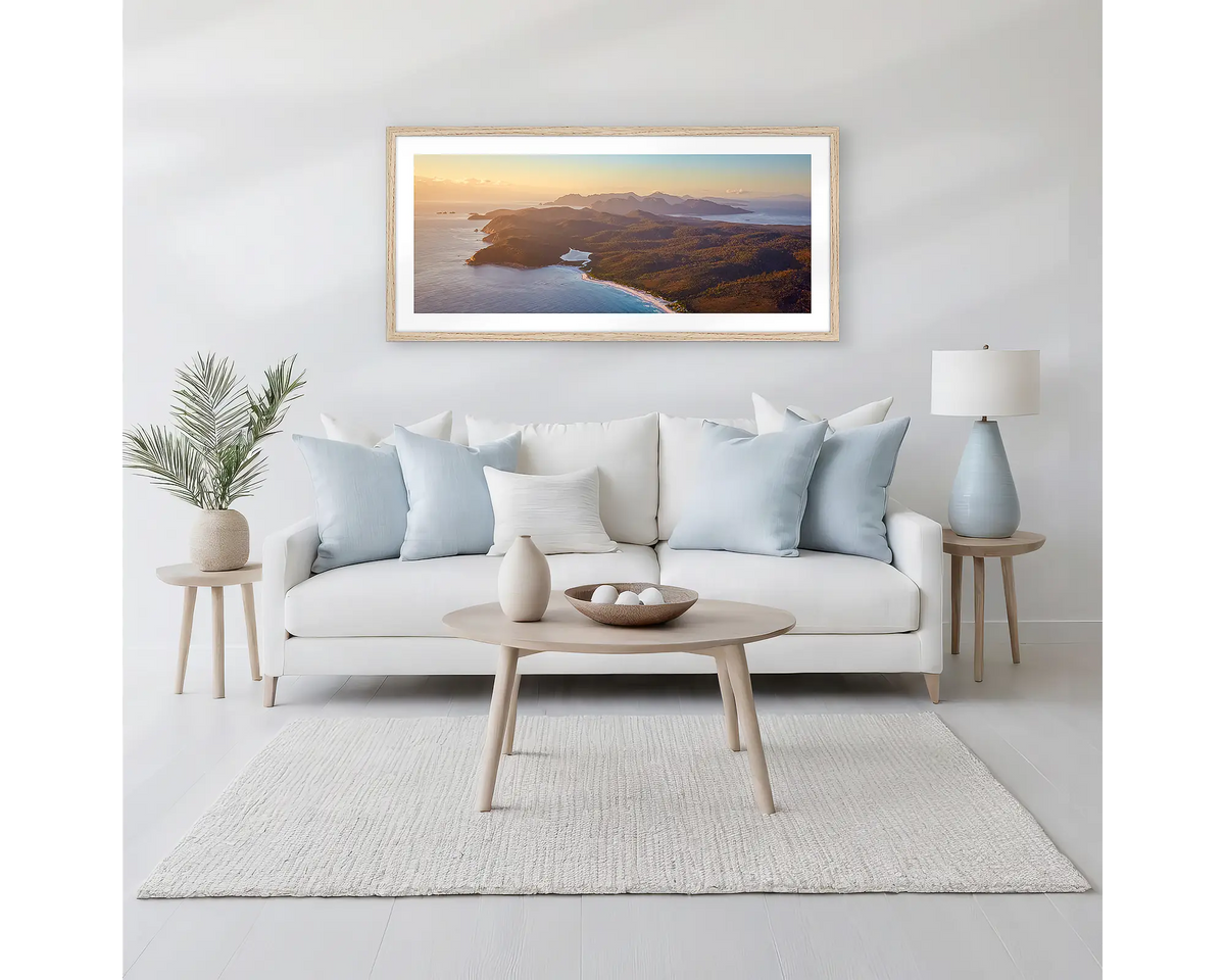 Dawn Over Freycinet. Framed wall art print of a sunrise over Freycinet National Park, with a timber frame hung above a neutral coloured couch. 