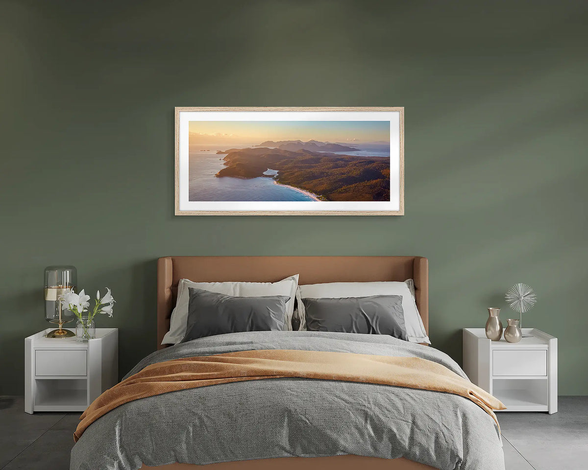Dawn Over Freycinet. Framed wall art print of a sunrise over Freycinet National Park, with a timber frame hung on a green wall above a bed. 