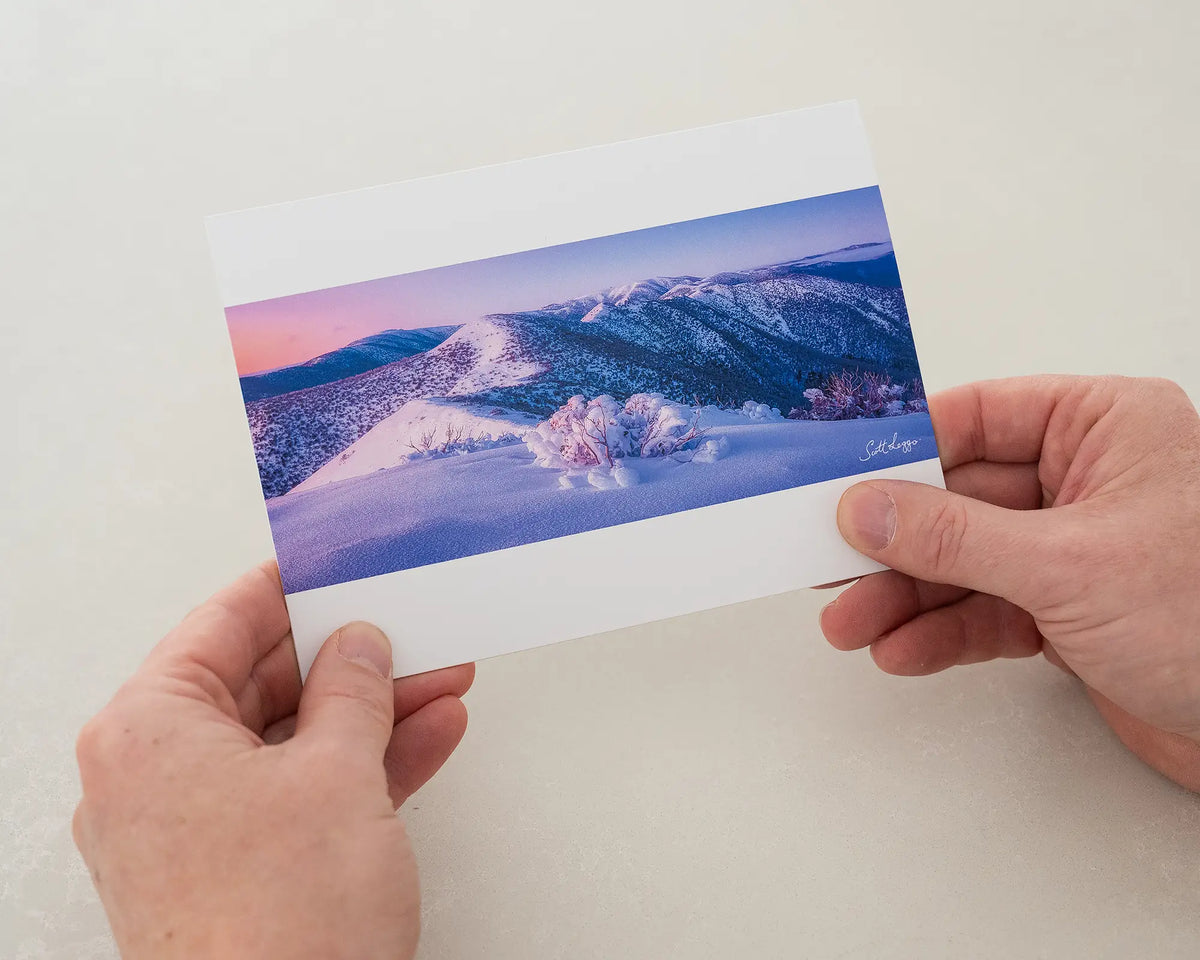 Distance greeting card of sunrise over Victorian alps, being held in two hands.