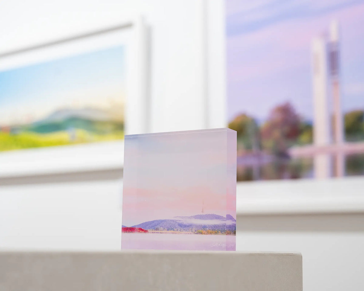 Dreamy Canberra. Acrylic block soft pink sky over Lake Burley Griffin, on gallery desk with Canberra wall art in background.